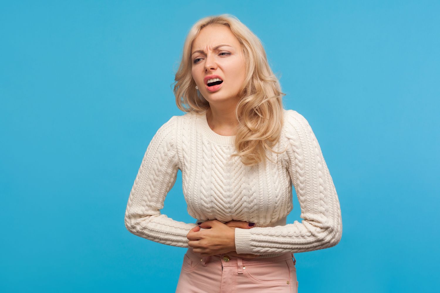 Upset blond woman screaming holding her belly, suffering from terrible acute pain